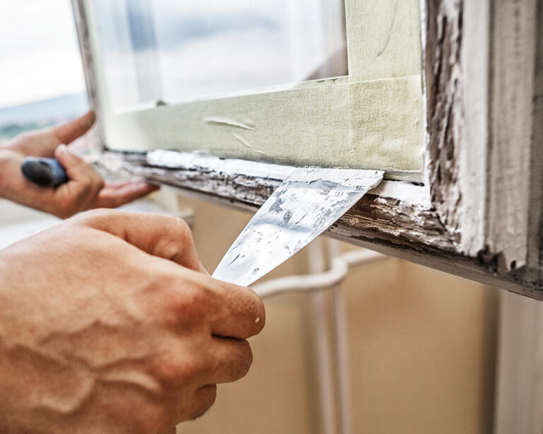 Glazier striking fresh linseed putty into a timber window rebate with a putty knife